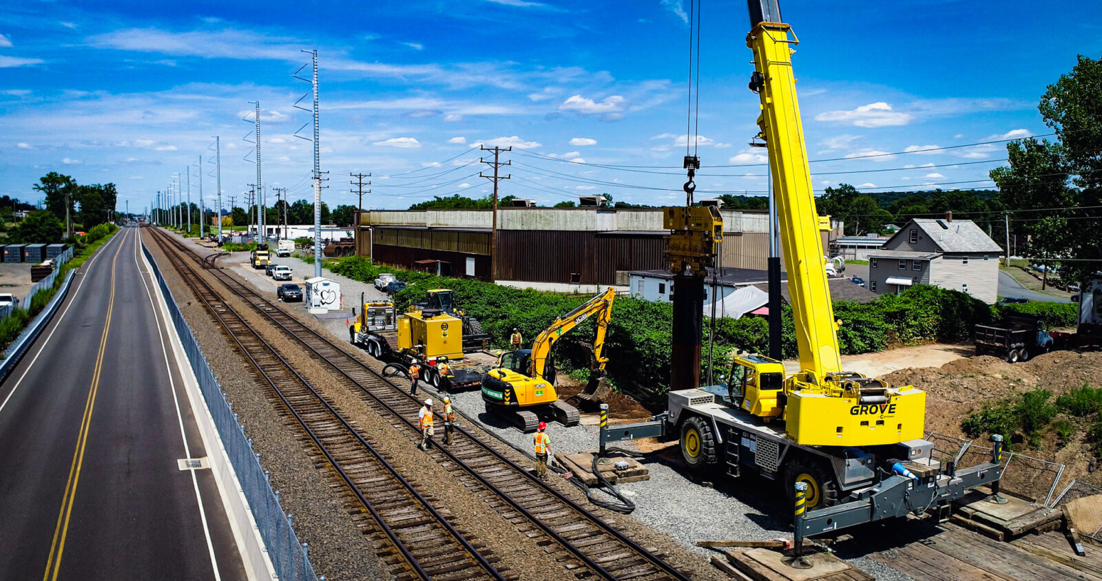 Yellow crane, excavator and truck with trailer beside a road and railway