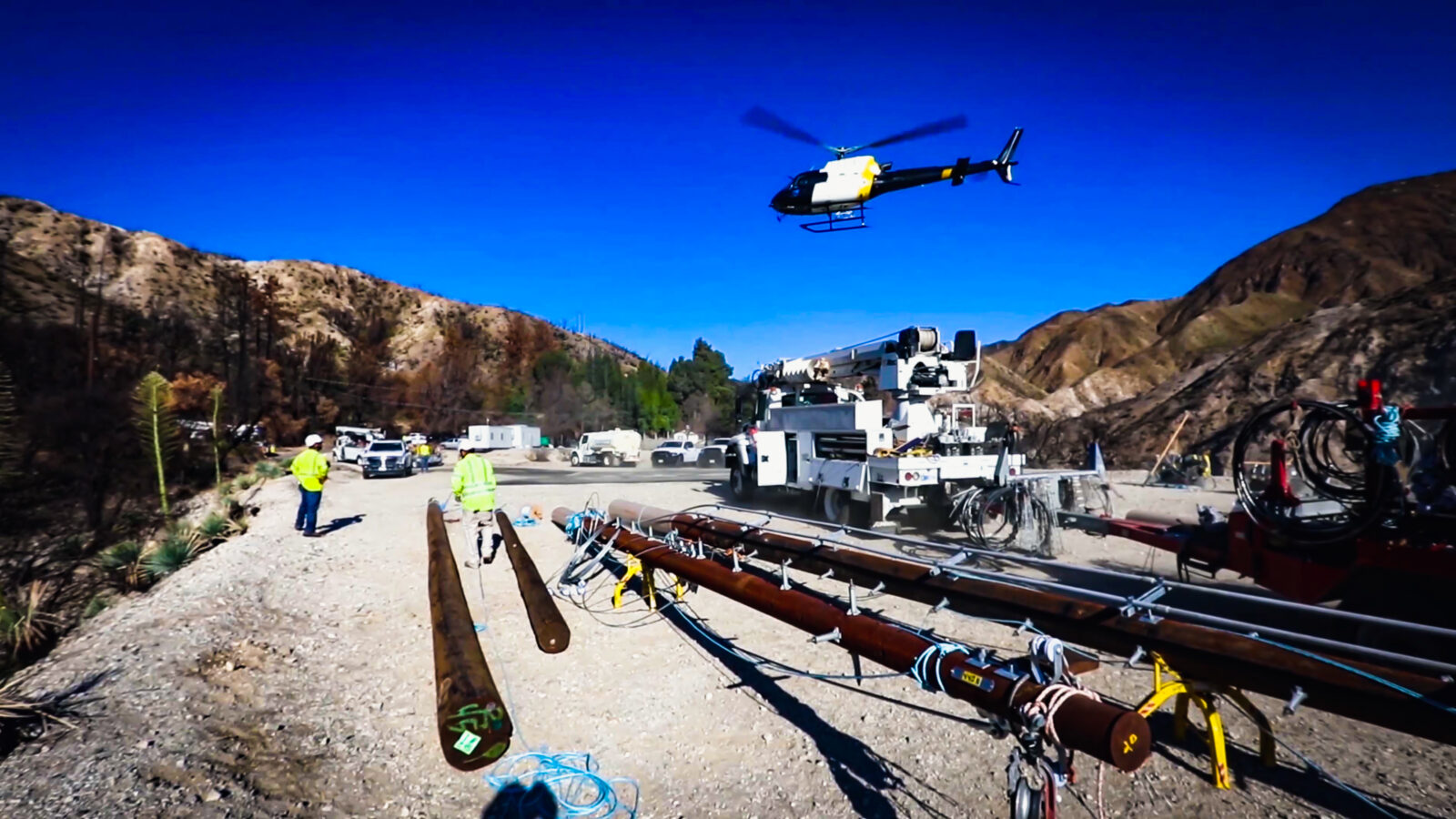 A helicopter flies above an area where power poles lay on the ground waiting for installation in California.